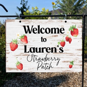 Könnte beinhalten: Willkommensschild zu Laurens Erdbeerfeld mit einem weiß getünchten Holzhintergrund und roten Erdbeeren.