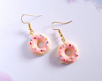 May include: A pair of gold dangle earrings featuring pink glazed donut charms with colourful sprinkles.