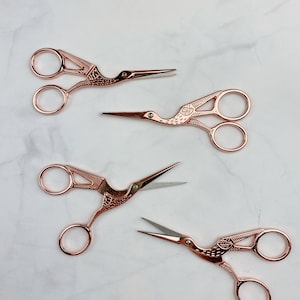 May include: Four rose gold scissors with a bird design. The scissors have a pointed tip and a small loop at the end of the handle.