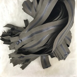 May include: A pile of dark green zipper tape with black teeth. The zippers are all the same length and are bundled together.