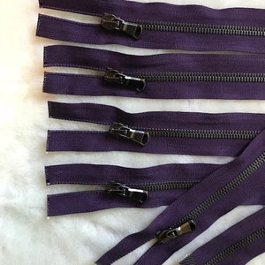 May include: A set of five purple zippers with black metal sliders. The zippers are all the same length and have a fine, textured fabric.