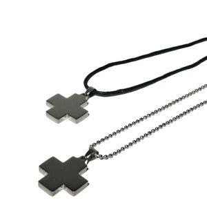 May include: Two silver cross pendants on chains. One pendant is on a black cord, the other is on a silver chain.