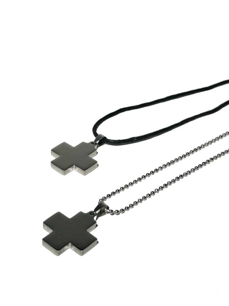 May include: Two silver cross pendants on chains. One pendant is on a black cord, the other is on a silver chain.