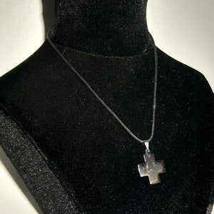 May include: A silver cross pendant necklace on a black cord.