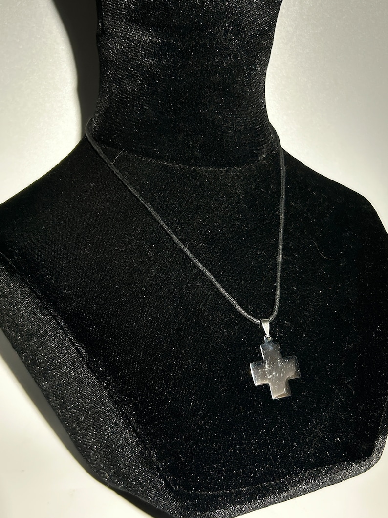 May include: A silver cross pendant necklace on a black cord.