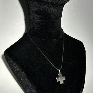 May include: A silver cross pendant necklace on a black cord, displayed on a black velvet mannequin bust.