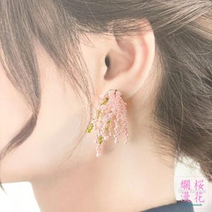 以下が含まれることがあります： ピンクとグリーンのビーズイヤリング。イヤリングは、小さな半透明のピンク色のビーズと、小さな銀色のベースから吊り下げられたいくつかの緑色のビーズで構成されています。イヤリングは揺れるように設計されています。