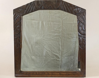 May include: A dark brown wooden mirror with an ornate carved frame. The frame features a geometric design with floral motifs.