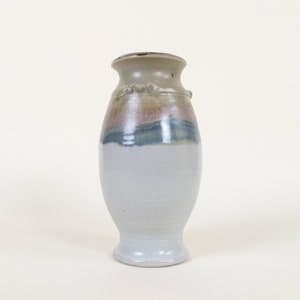 Peut inclure: Un petit vase en céramique blanche avec un bord brun et un glaçage bleu et rose. Le vase a un corps arrondi et une base évasée.