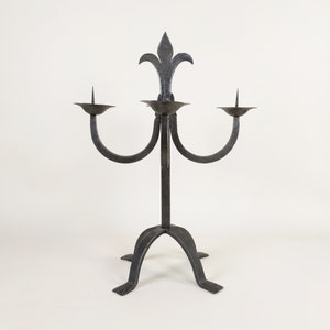 May include: A black metal candelabra with three candle holders and a decorative fleur-de-lis design at the top.