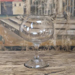 Könnte beinhalten: Eine klare Glasschale mit einem breiten, kugelförmigen Körper und einer schmalen Öffnung an der Oberseite, die von einem schlanken Stiel und einem runden Fuß getragen wird. Das Glas ist transparent, glatt und reflektiert das Licht.