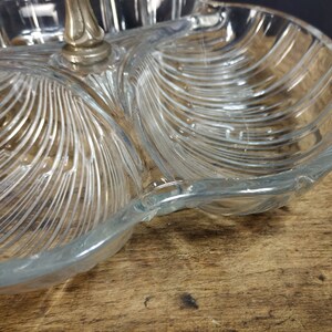 May include: A clear glass serving dish with three sections. The dish has a decorative, ribbed pattern and a silver metal handle.