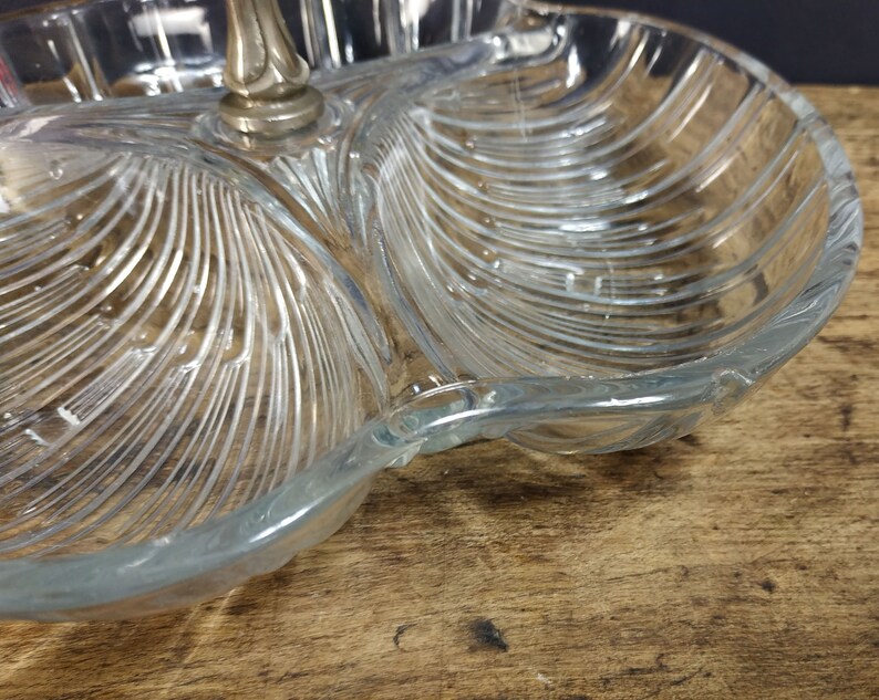May include: A clear glass serving dish with three sections. The dish has a decorative, ribbed pattern and a silver metal handle.