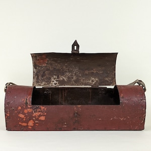 Puede incluir: Una caja vintage de metal rojo con una tapa con bisagras y un asa de metal. La caja tiene un acabado desgastado y oxidado y está asegurada con remaches de metal.