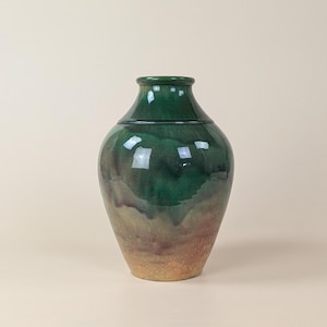 May include: A green ceramic vase with a brown glaze at the bottom. The vase has a rounded body and a narrow neck.