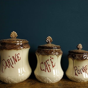 Könnte beinhalten: Set aus drei antiken Keramikbehältern mit braunen und weißen Blumenmustern. Die Behälter sind mit "Farine", "Cafe" und "Poivre" beschriftet.