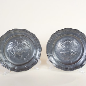 Deux anciens plats décoratifs en métal en étain français avec des animaux exotiques et des décorations de fleur de lys et de couronne avec la marque de fabricants