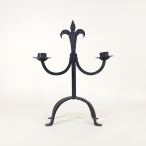 May include: Black wrought iron candle holder with a fleur-de-lis design and two candle arms.