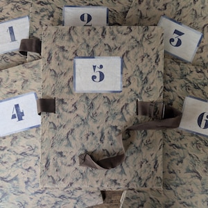May include: A patterned storage box with a brown strap and numbered cards. The box and cards have a marbled, blue and beige design. The cards are numbered 1 through 6 in a dark blue font.