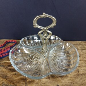 May include: A clear glass serving dish with three sections and a silver handle. The dish has a decorative, ribbed pattern.