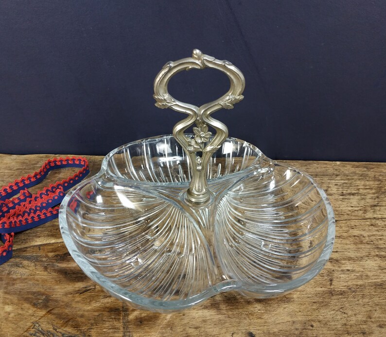 May include: A clear glass serving dish with three sections and a silver handle. The dish has a decorative, ribbed pattern.