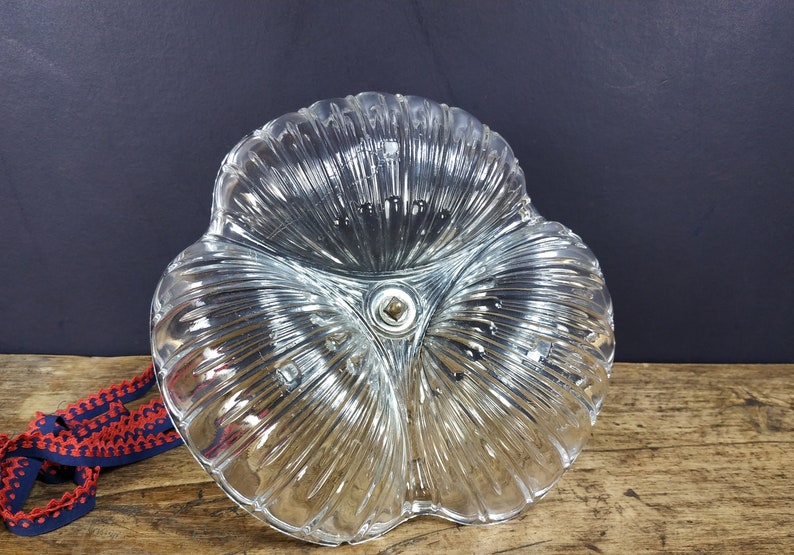 May include: A clear glass dish with a three-leaf clover design. The dish has a textured, ribbed surface and a small metal knob in the center.