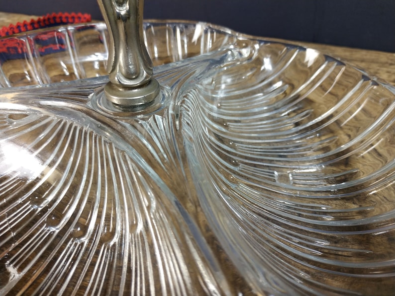 May include: A clear glass serving dish with three sections and a silver handle. The dish has a decorative, ribbed pattern.