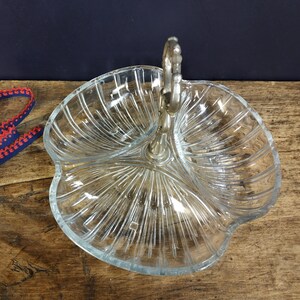 May include: A clear glass serving dish with three sections and a silver handle. The dish has a decorative, ribbed pattern.