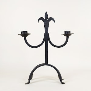 May include: Black metal candle holder with a decorative fleur-de-lis design and two candle arms.