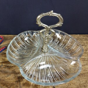May include: A clear glass serving dish with three sections and a silver handle. The dish has a decorative, ribbed pattern.