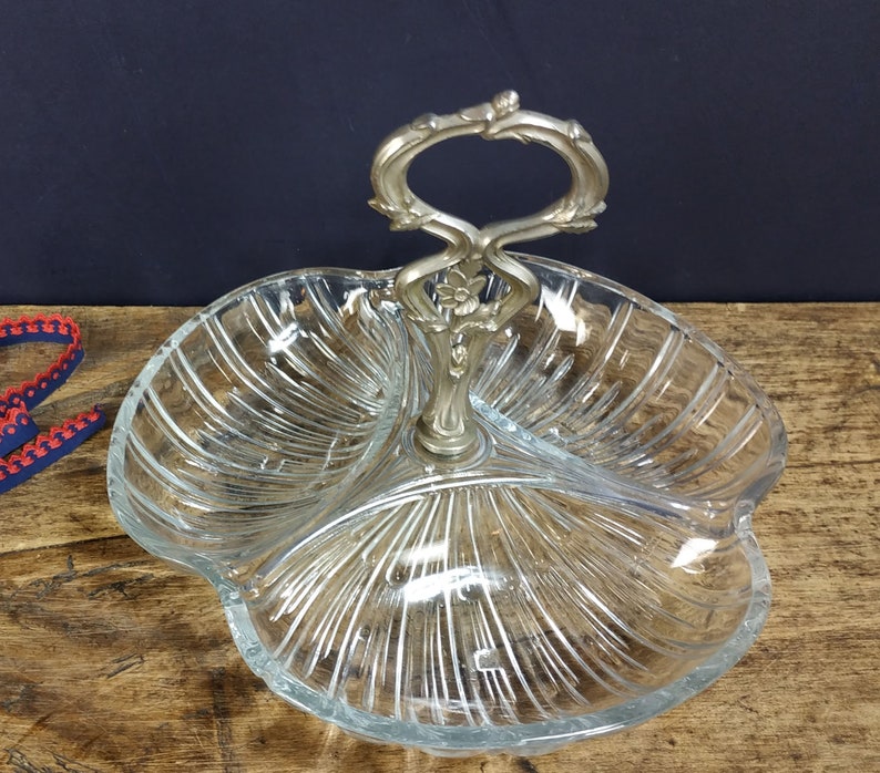 May include: A clear glass serving dish with three sections and a silver handle. The dish has a decorative, ribbed pattern.