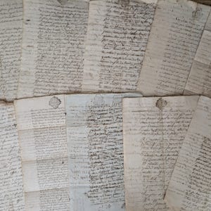 Op de afbeelding: Een verzameling oude, handgeschreven documenten met vervaagde inkt. De papieren zijn in een verspreid patroon gerangschikt, met ingewikkelde handschriften en mogelijke zegels. De algemene toon suggereert historische betekenis en een vintage esthetiek.