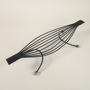 May include: A black metal wire sculpture with a curved, elongated shape and two round silver accents at the ends.