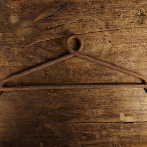 May include: A rusty metal hook with a rounded top and two pointed ends. The hook is on a wooden surface.