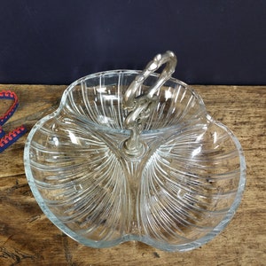 May include: A clear glass serving dish with three sections and a silver handle. The dish has a scalloped edge and a ribbed design.