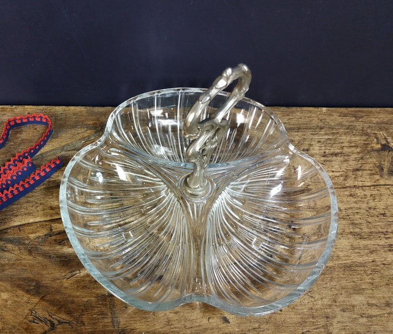 May include: A clear glass serving dish with three sections and a silver handle. The dish has a scalloped edge and a ribbed design.