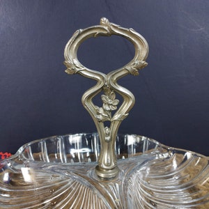 May include: A clear glass serving dish with three sections and a decorative silver handle. The handle is ornate and features a floral design.