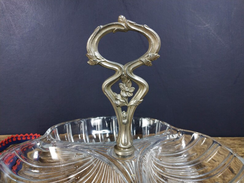 May include: A clear glass serving dish with three sections and a decorative silver handle. The handle is ornate and features a floral design.
