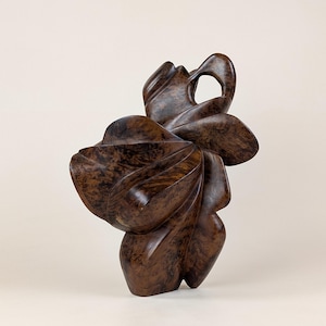 Könnte beinhalten: Eine braune Holzskulptur mit einem abstrakten, fließenden Design. Die Skulptur weist geschwungene Linien und organische Formen mit einer strukturierten Oberfläche auf. Das Kunstwerk hat eine natürliche, erdige Ästhetik, passend für Heimdekoration oder Kunstsammlungen.