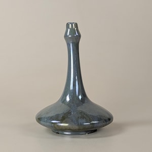 May include: A tall, iridescent blue-green ceramic vase with a flared base and a slender, elongated neck. The vase has a glossy finish with subtle color variations, creating a unique, artistic appearance. The vase is a decorative item.