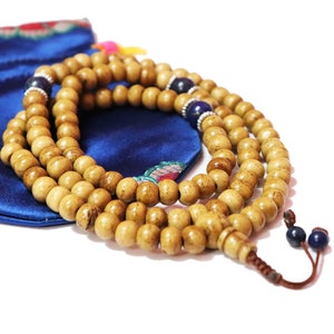 May include: A wooden mala bead necklace with blue beads and a tassel. The necklace is wrapped around a blue satin pouch with floral embroidery.