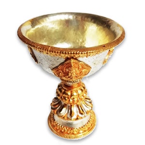 May include: A silver and gold butter lamp with intricate designs. The lamp has a round bowl with a decorative base.