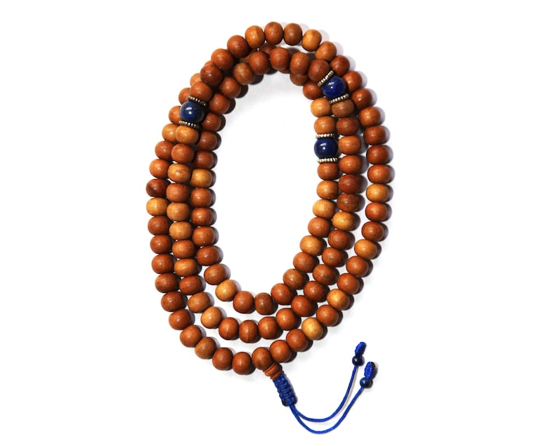 May include: A brown wooden mala bead necklace with blue gemstone accents. The necklace is strung with a blue cord and has a tassel at the end.