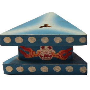 May include: A blue wooden triangular incense burner with a white and red painted design of a mythical creature with flames. The burner has a hole in the top for incense sticks.