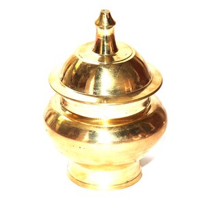 May include: A gold metal container with a lid. The container has a round body and a domed lid with a small finial on top.