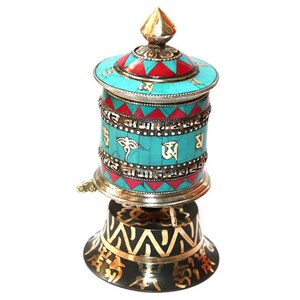 May include: A turquoise and red prayer wheel with gold accents and a black base with gold lettering. The prayer wheel is decorated with intricate patterns and symbols.