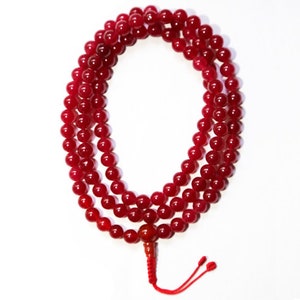 Puede incluir: Un mala, o cuentas de oración, de piedras preciosas rojas con un borla. Las cuentas son redondas y lisas, y la borla está hecha de cordón rojo.