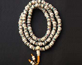 May include: A white bone mala with turquoise, red, and black accents. The mala is made of 108 beads and has a tassel.