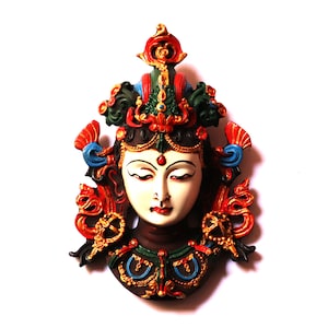 May include: A colorful, ornate mask depicting a deity with a serene expression. The mask is painted in shades of red, blue, green, gold, and white, with intricate details and a crown-like headdress.