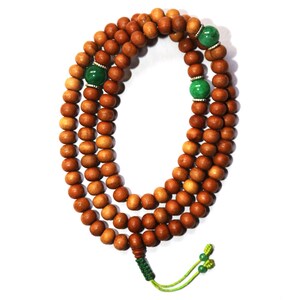 May include: A brown wooden mala bead necklace with green gemstone accents. The necklace is made of 108 beads and has a tassel at the end.